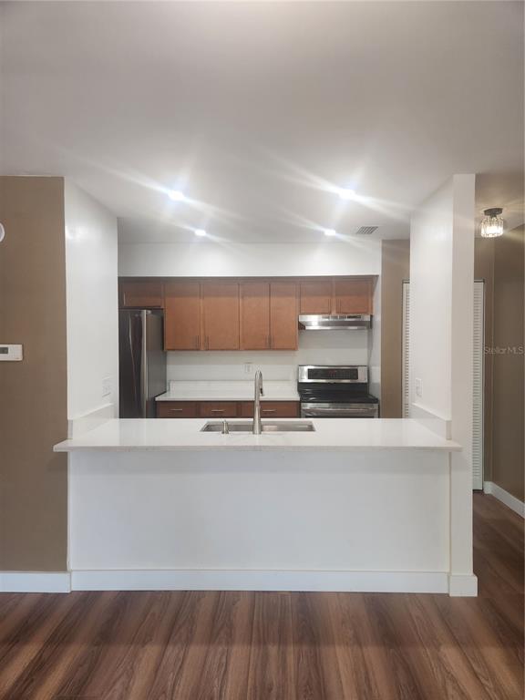 A kitchen with wood cabinets, stainless steel appliances, and a white breakfast bar countertop — 13608 S VILLAGE DRIVE UNIT 6204, TAMPA, FL