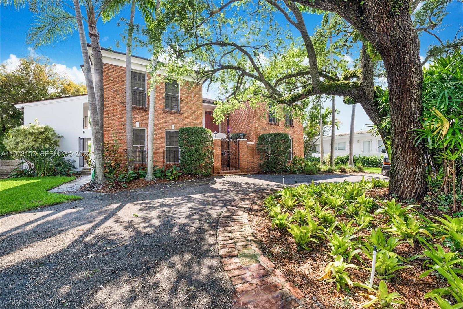 A two-story brick house features a paved driveway, mature trees, and a gated entrance — 1265 S Alhambra Cir # A, Coral Gables FL 33146, CORAL GABLES, FL