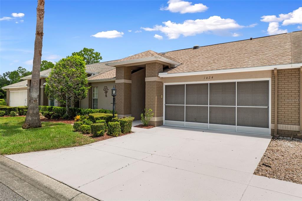 A single-story house with a tan brick facade, a screened garage, and a palm tree — 1424 PINEWOOD HILLS COURT, SPRING HILL, FL