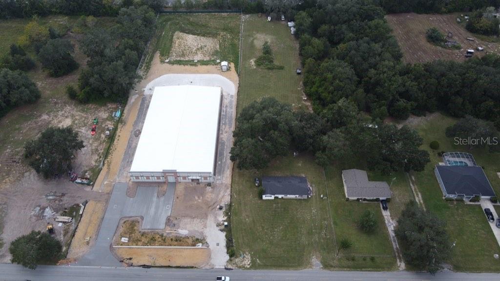 An aerial view shows a large warehouse building next to residential houses and wooded lots — 35433 MICRO RACETRACK ROAD, FRUITLAND PARK, FL