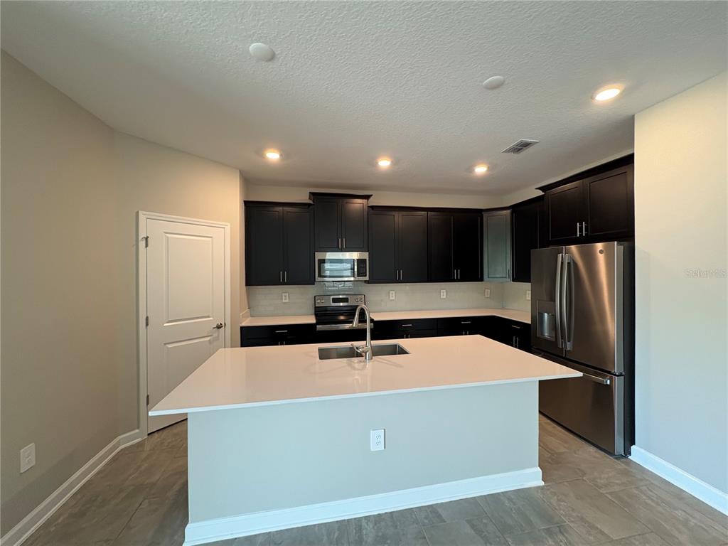 A kitchen features dark cabinets, stainless steel appliances, a white island, and light-colored flooring — 2836 CAMDEN WAY, DAVENPORT, FL