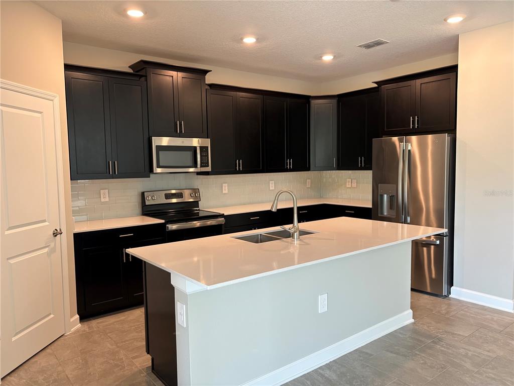 A kitchen features dark cabinets, stainless steel appliances, a white island, and light tile flooring — 2836 CAMDEN WAY, DAVENPORT, FL