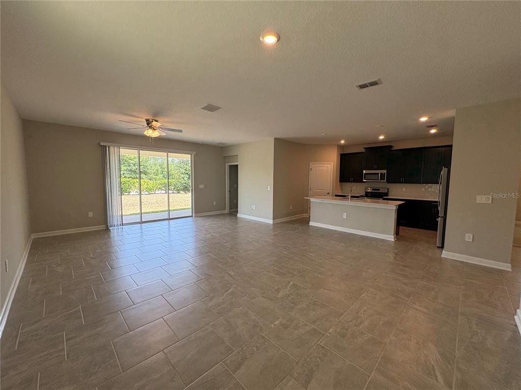 An open-concept living area features tile flooring, a kitchen with dark cabinets, and sliding doors — 2836 CAMDEN WAY, DAVENPORT, FL
