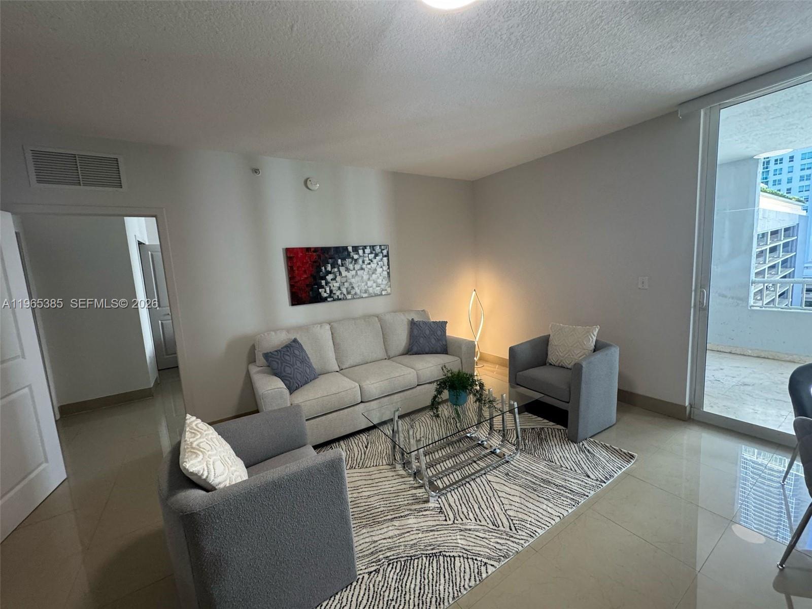 A living room features a light-colored sofa, two grey armchairs, a glass coffee table, and a balcony — 170 SE 14th St # 1108, Miami FL 33131, MIAMI, FL