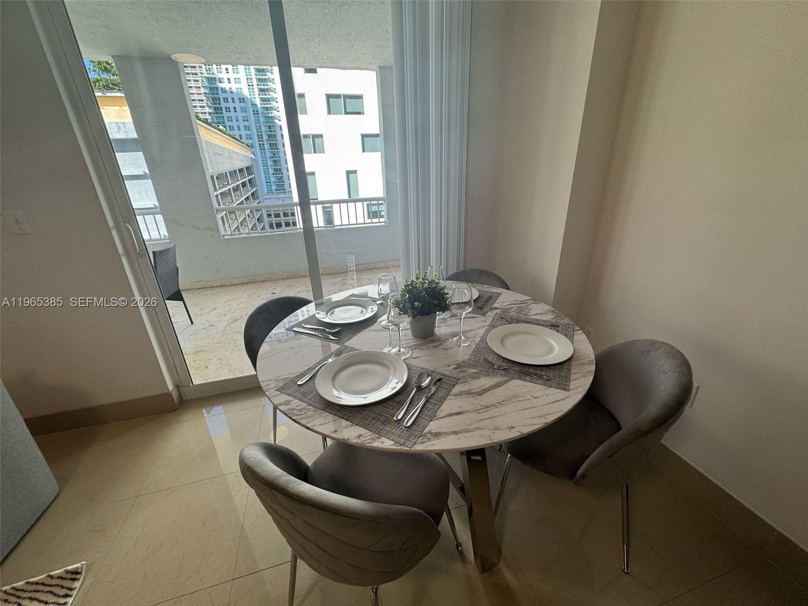 A round marble dining table with four grey chairs sits near a balcony sliding door — 170 SE 14th St # 1108, Miami FL 33131, MIAMI, FL