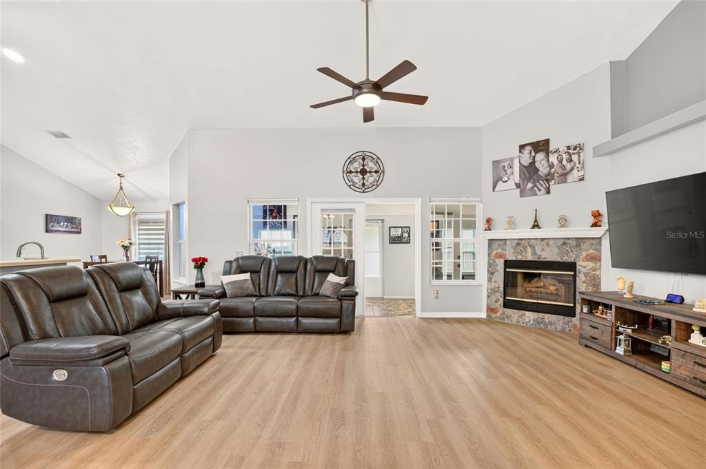 A living room features light wood flooring, dark leather sofas, a stone fireplace, and a ceiling fan — 11213 NW 34TH AVENUE, GAINESVILLE, FL