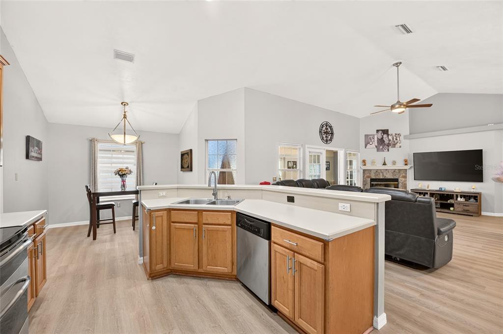 A kitchen with wood cabinets and a breakfast nook overlooks a living room with vaulted ceilings — 11213 NW 34TH AVENUE, GAINESVILLE, FL
