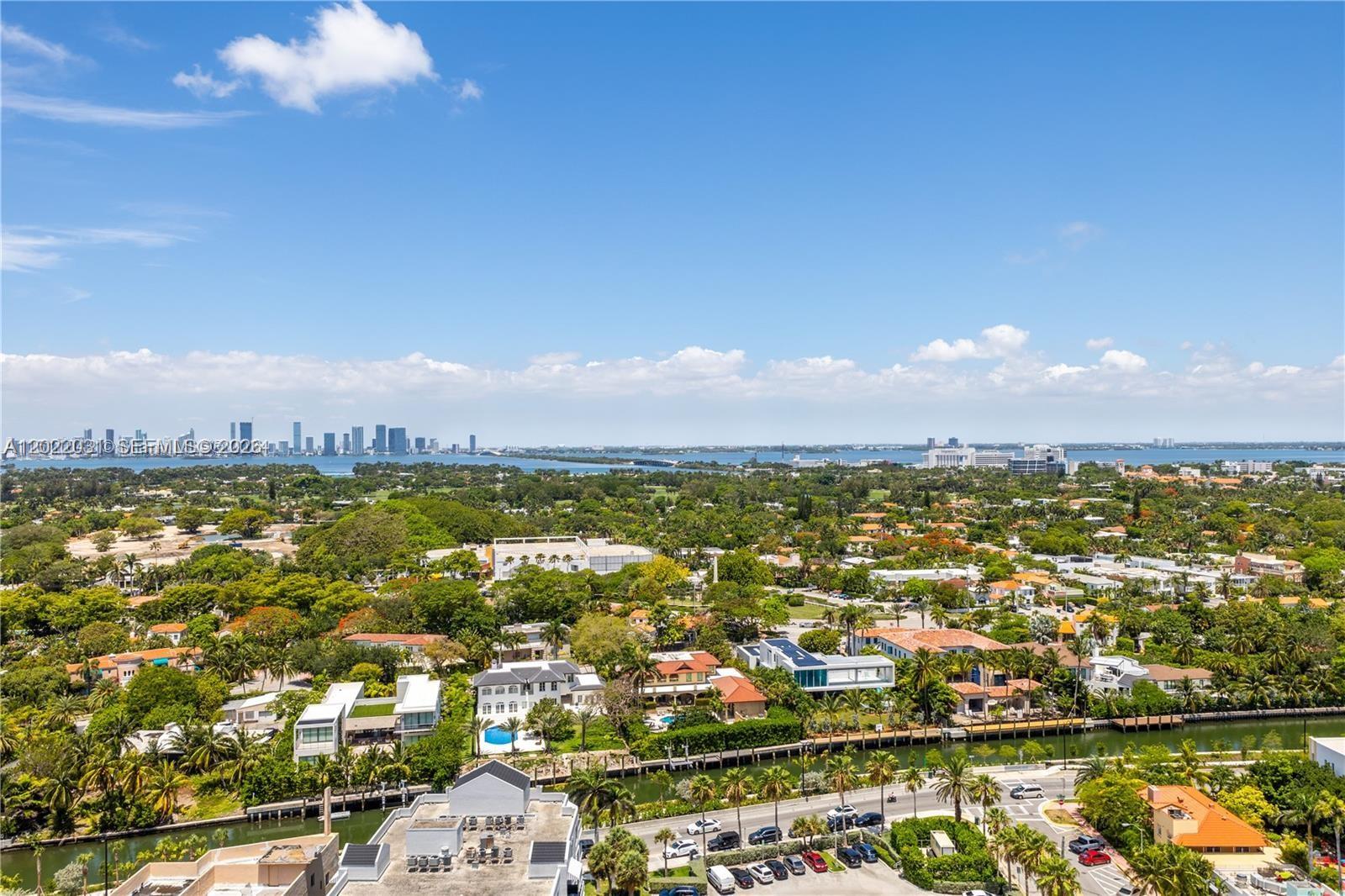 An aerial view shows a suburban neighborhood with houses, a canal, and a distant skyline — 2655 Collins Ave # 2302, Miami Beach FL 33140, MIAMI BEACH, FL