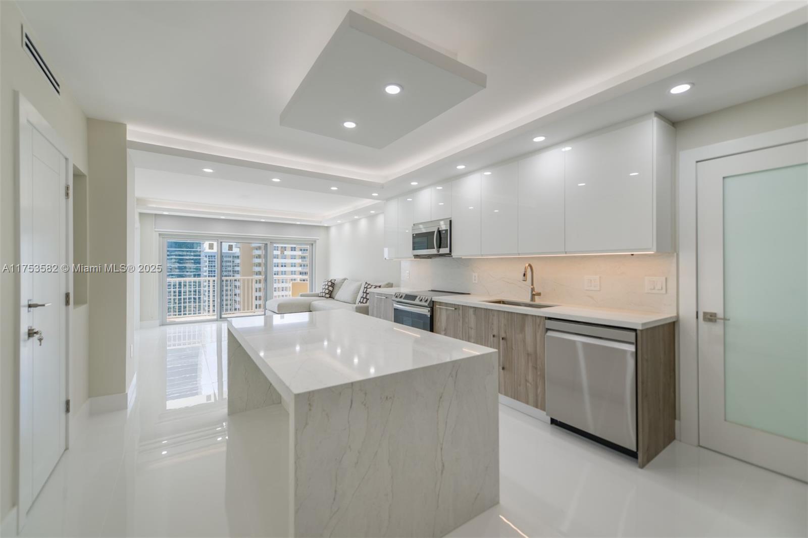A modern kitchen features white glossy cabinets, wood-toned lower cabinets, and a marble waterfall island — 1950 S Ocean Dr # 20L, Hallandale Beach FL 33009, HALLANDALE BEACH, FL