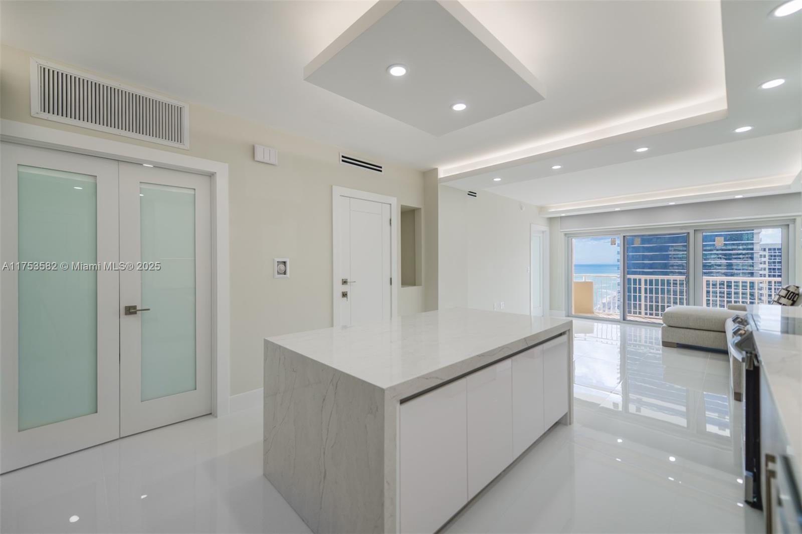 A modern kitchen features a marble-topped island, white cabinetry, and a view of the ocean — 1950 S Ocean Dr # 20L, Hallandale Beach FL 33009, HALLANDALE BEACH, FL