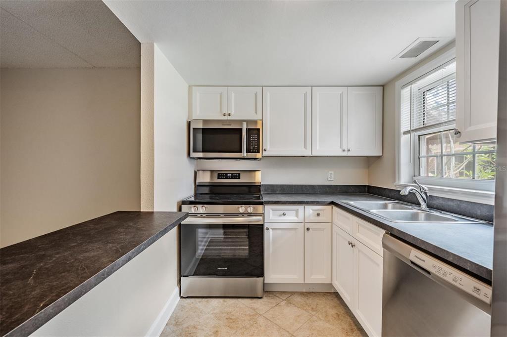 A kitchen features white cabinets, stainless steel appliances, and dark countertops with a tile floor — 8565 12TH WAY N UNIT A, ST PETERSBURG, FL
