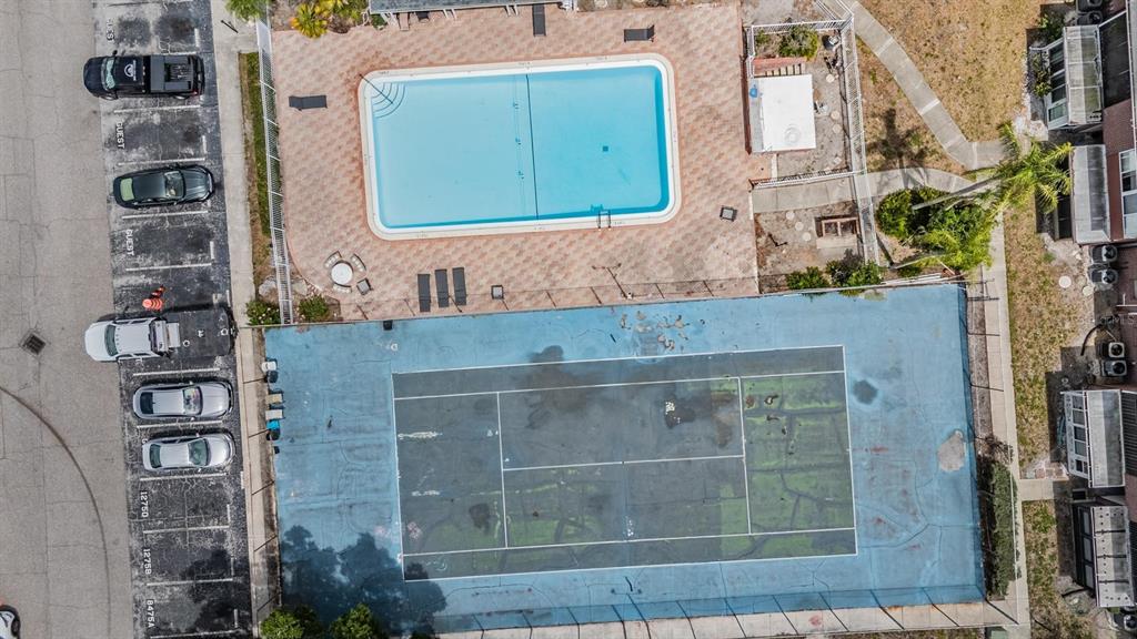 An aerial view shows a rectangular swimming pool and a tennis court next to parking — 8565 12TH WAY N UNIT A, ST PETERSBURG, FL