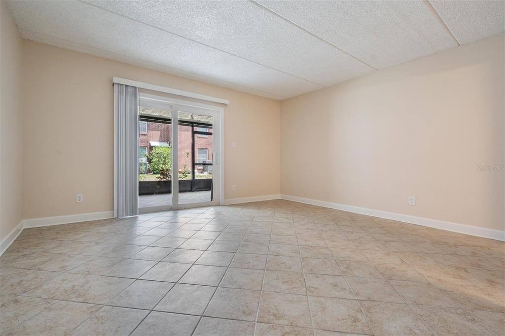 An empty room with beige walls, tiled floors, and a sliding glass door to a patio — 8565 12TH WAY N UNIT A, ST PETERSBURG, FL