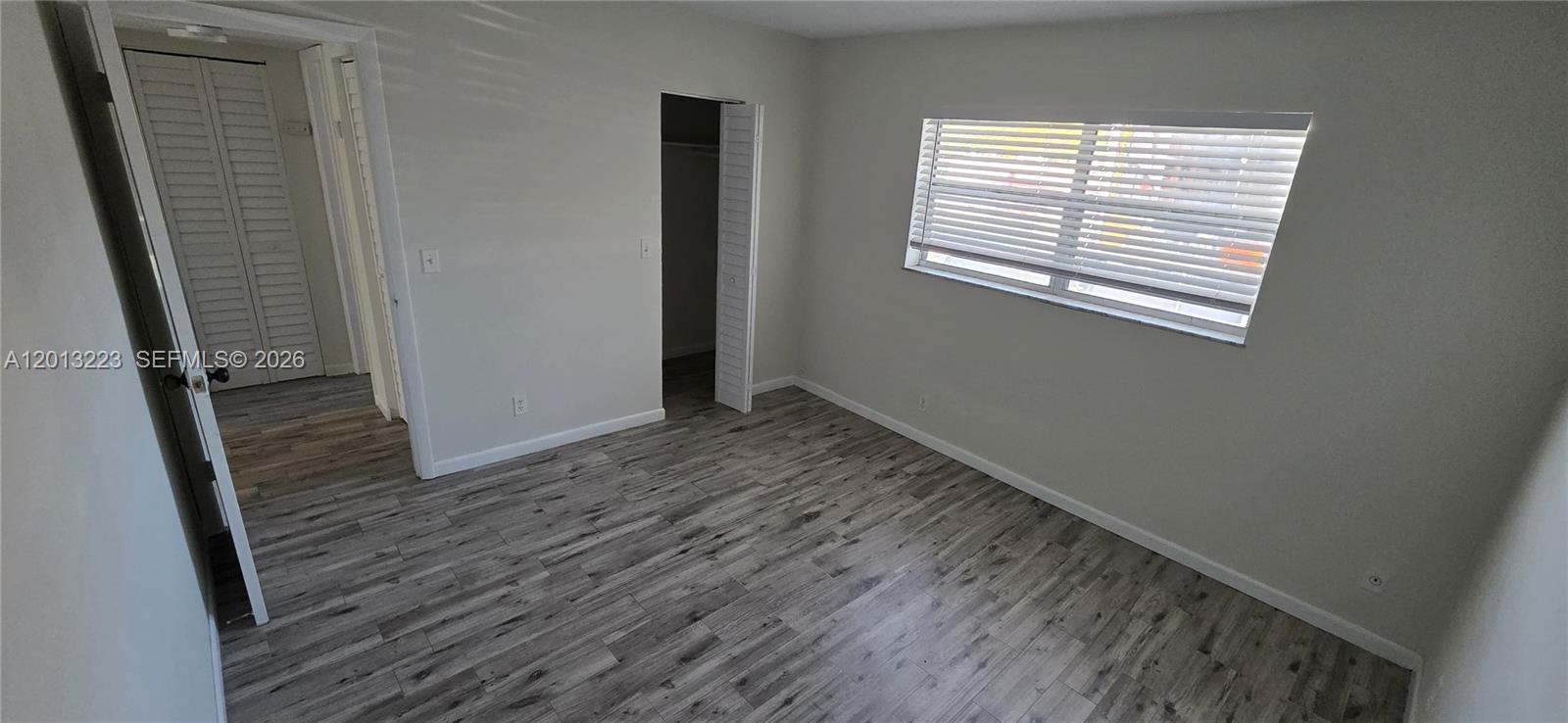 An empty bedroom features gray wood-look flooring, light gray walls, and a window with blinds — 30 SE 4th Ave # 115, Hallandale Beach FL 33009, HALLANDALE BEACH, FL