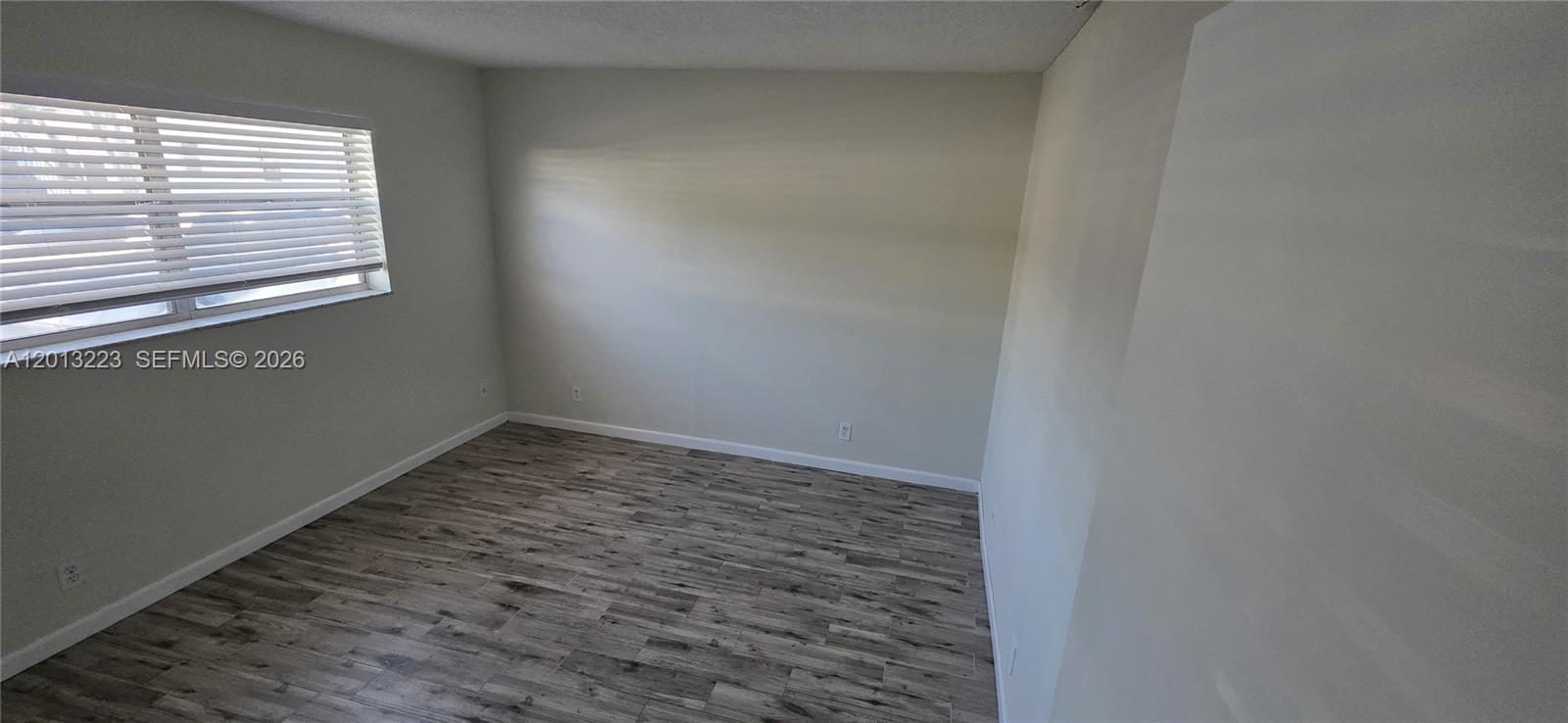 An empty room features light-colored walls, a window with blinds, and wood-look flooring — 30 SE 4th Ave # 115, Hallandale Beach FL 33009, HALLANDALE BEACH, FL