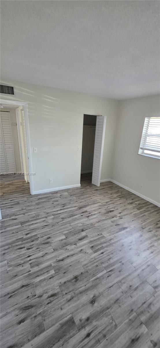 An empty bedroom features light-colored walls, a closet with louvered doors, and gray wood-look flooring — 30 SE 4th Ave # 115, Hallandale Beach FL 33009, HALLANDALE BEACH, FL