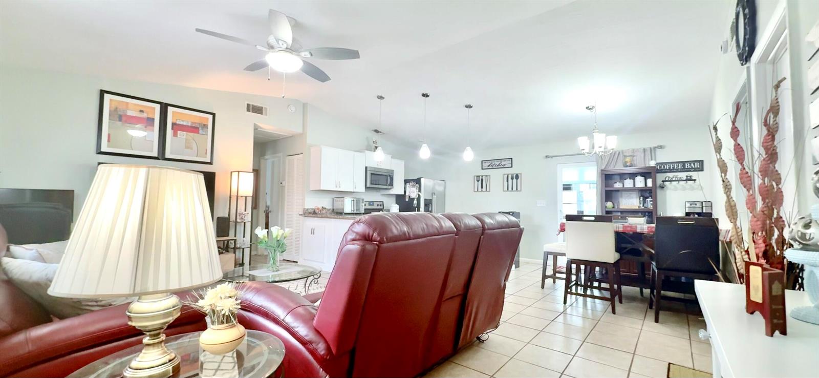 An open-concept living and dining area features tile flooring, a red sofa, and white cabinetry — 617 Thuringer Street NW, Palm Bay FL 32907, PALM BAY, FL