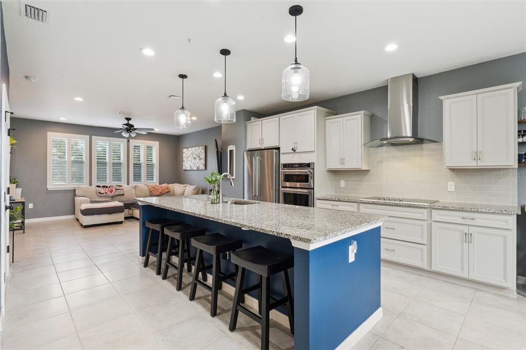A kitchen with a blue island, granite countertops, white cabinets, and an adjacent living area — 476 PORTICO COURT, OVIEDO, FL