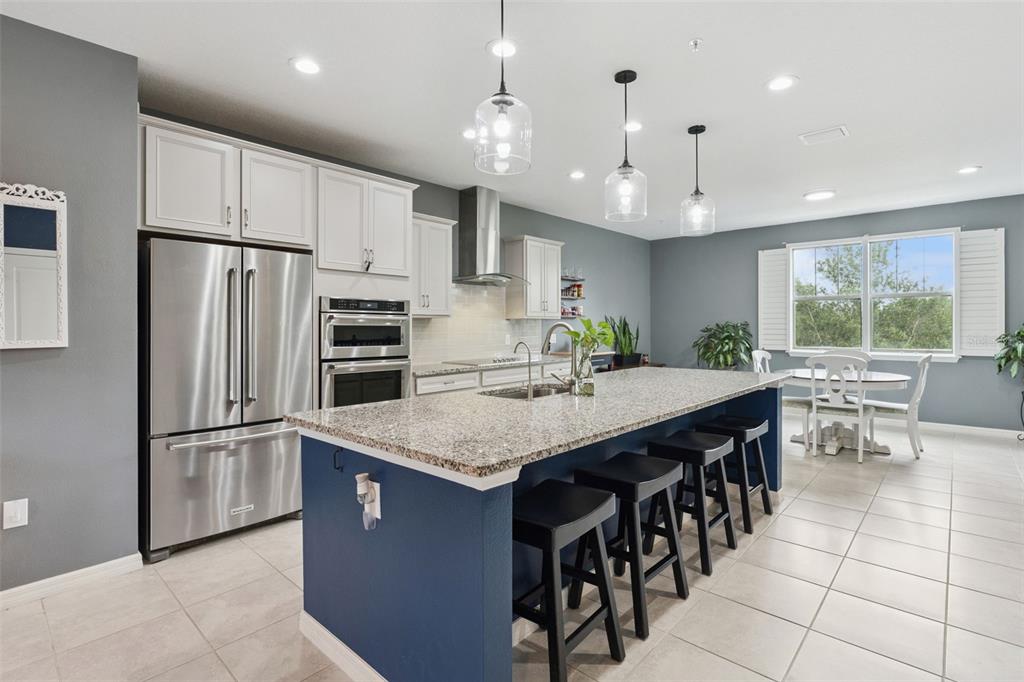 A kitchen features a blue island with bar stools, white cabinets, and stainless steel appliances — 476 PORTICO COURT, OVIEDO, FL