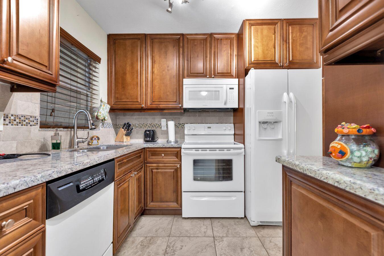 A kitchen with wood cabinets, granite countertops, white appliances, and a tiled backsplash — 6850 Royal Palm Boulevard # 106g, Margate FL 33063, MARGATE, FL