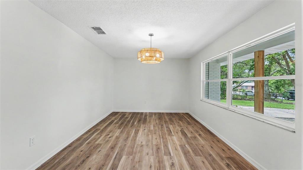 An empty dining room features wood-look flooring, white walls, and a round woven light fixture — 7209 GROVE WAY, LAKELAND, FL
