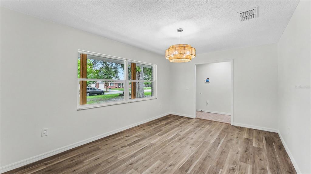 An empty dining room features light wood-look flooring, white walls, and a round drum chandelier — 7209 GROVE WAY, LAKELAND, FL