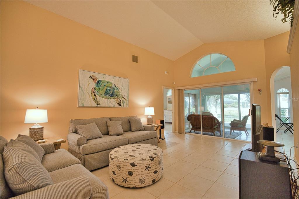 A living room with vaulted ceilings, tile floors, a sofa, and a patterned ottoman — 1191 HARBOR TOWN WAY, VENICE, FL