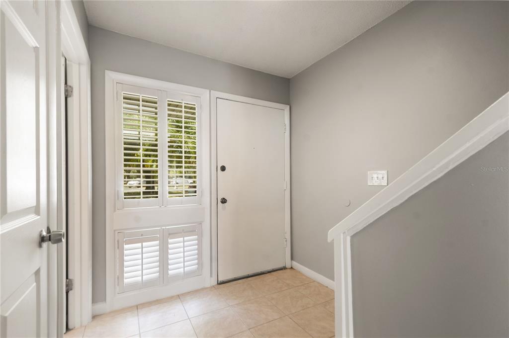 An entryway features a white door, plantation shutters, tiled flooring, and a staircase railing — 6114 PEREGRINE AVENUE UNIT D03, ORLANDO, FL