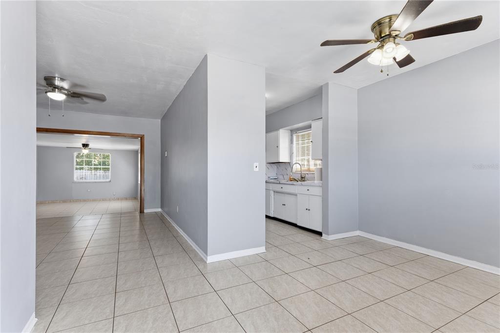A dining area with tile flooring leads into a kitchen with white cabinets — 998 W 68TH STREET, HIALEAH, FL