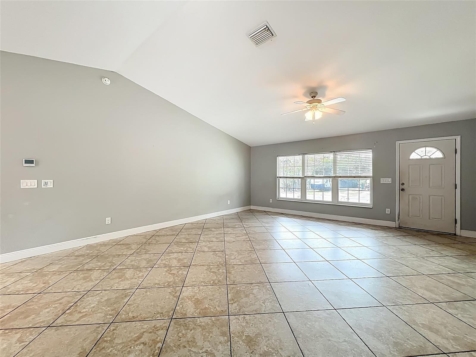 An empty living room features light gray walls, a vaulted ceiling, and beige tile flooring — 608 Masters Avenue, Wildwood FL 34785, WILDWOOD, FL