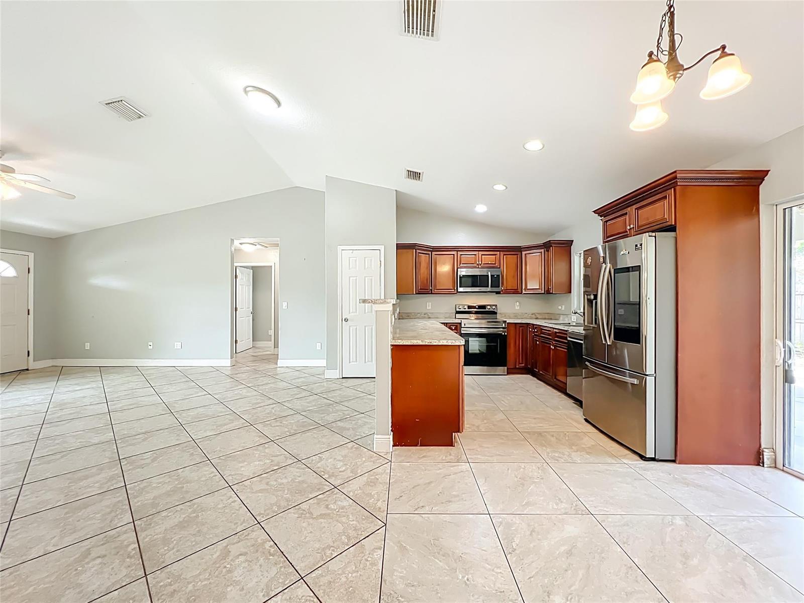 An open-concept kitchen features cherry wood cabinets, stainless steel appliances, and light-colored tile flooring — 608 Masters Avenue, Wildwood FL 34785, WILDWOOD, FL