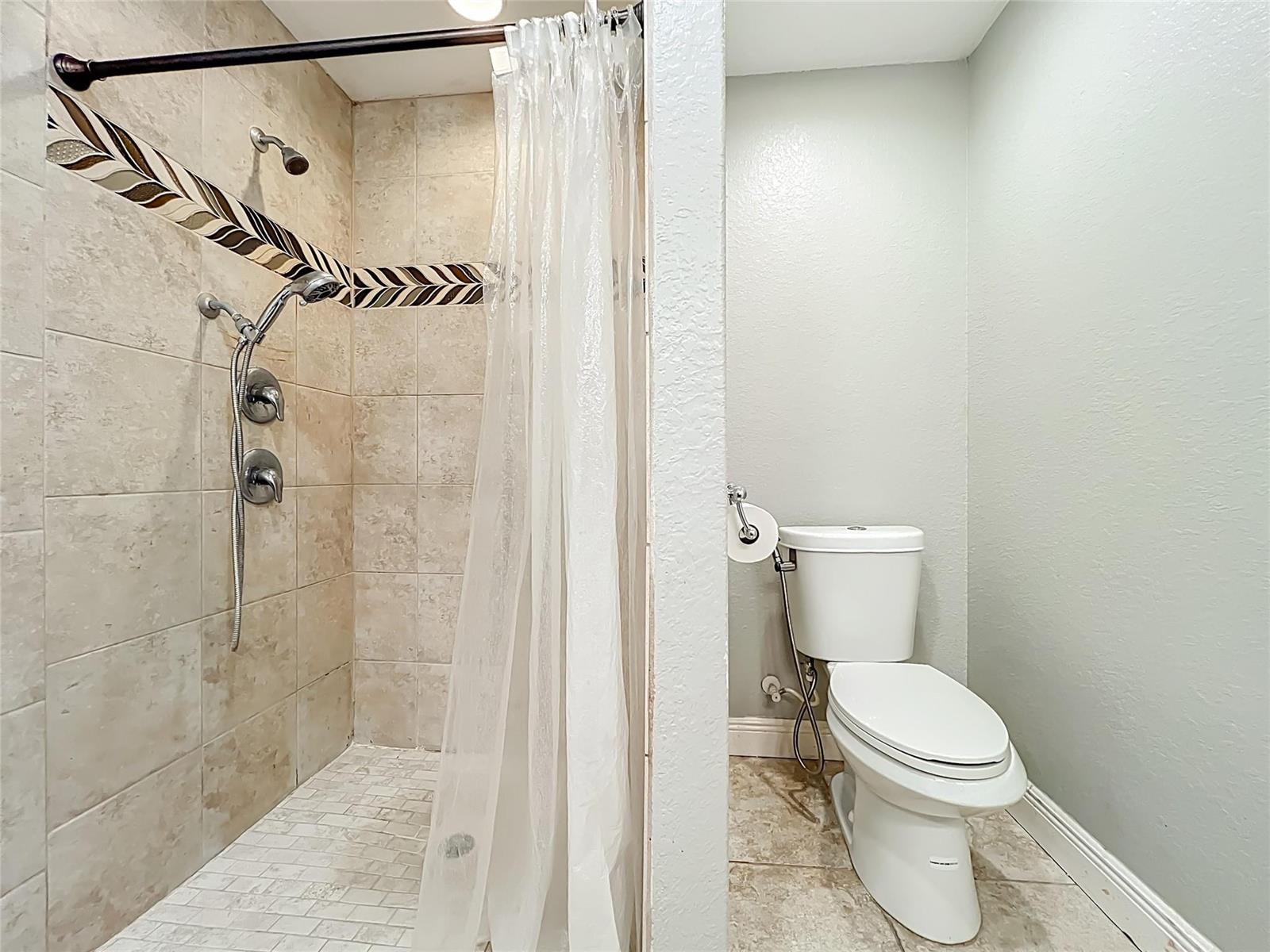 A bathroom features a tiled walk-in shower with a glass curtain next to a toilet — 608 Masters Avenue, Wildwood FL 34785, WILDWOOD, FL