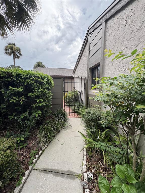 A concrete walkway leads to a metal gate between a house and a hedge — 635 WOODRIDGE DR, FERN PARK, FL