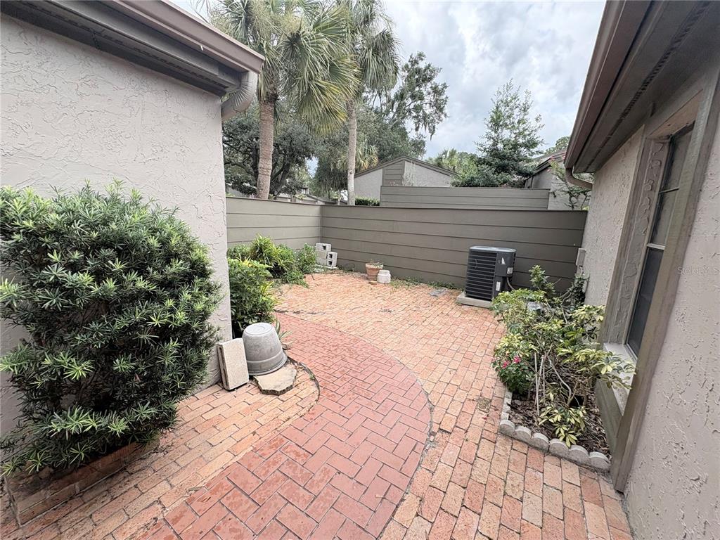 A brick patio sits between two stucco house walls with a privacy fence and landscaping — 635 WOODRIDGE DR, FERN PARK, FL