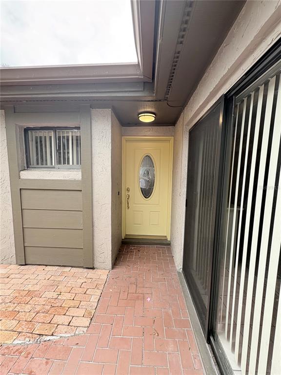 A brick patio leads to a yellow front door with an oval glass insert — 635 WOODRIDGE DR, FERN PARK, FL