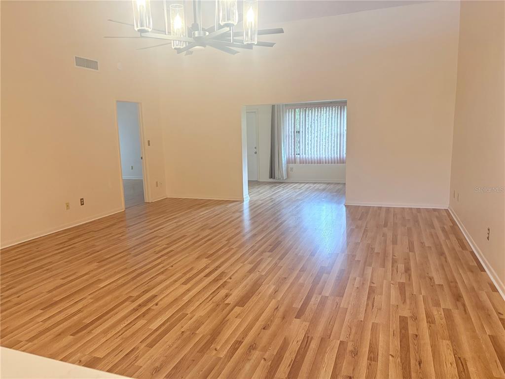A spacious living room features light wood-look flooring, high ceilings, and a modern chandelier — 635 WOODRIDGE DR, FERN PARK, FL