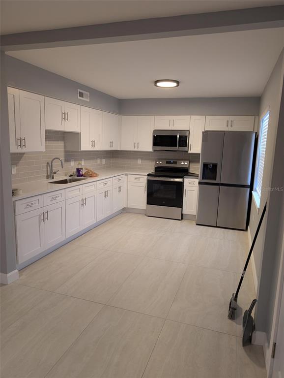 A kitchen features white cabinetry, stainless steel appliances, light countertops, and large floor tiles — 4416 N CLARK AVENUE UNIT 4, TAMPA, FL