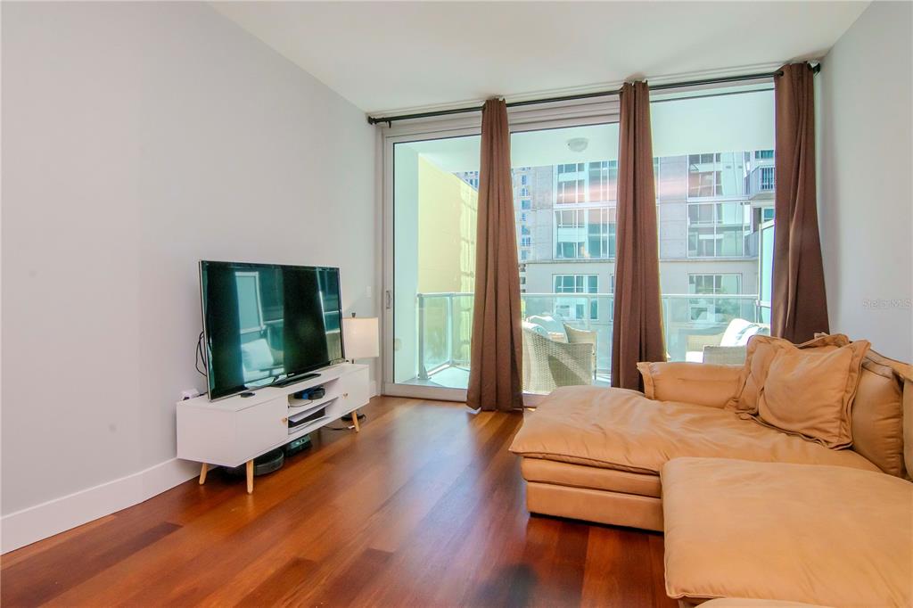 A living room features hardwood floors, a sectional sofa, a television, and a balcony entrance — 111 N 12TH STREET UNIT 1523, TAMPA, FL