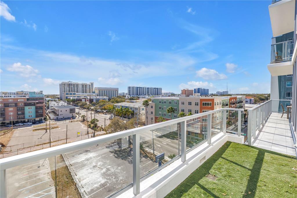A balcony with glass railings and artificial turf overlooks a city street and buildings — 777 3RD AVENUE N UNIT 708, ST PETERSBURG, FL