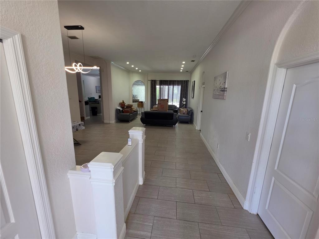 A long, tiled hallway leads into an open living area with dark furniture and curtains — 271 PETREL TRAIL, BRADENTON, FL