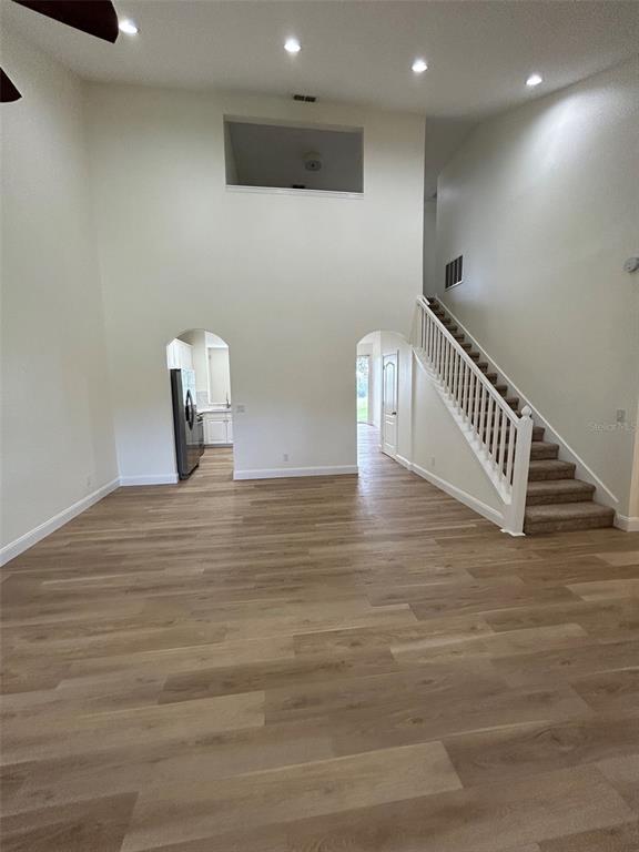 A living room with light wood-look flooring, a staircase, and arched doorways leading to a kitchen — 34322 TUSCANY AVENUE, SORRENTO, FL