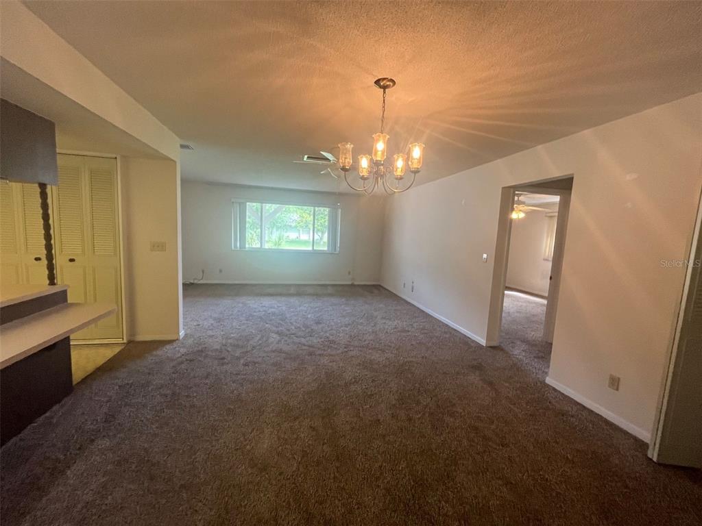 A carpeted living room features a chandelier, a ceiling fan, and a large window — 13 COURTNEY PLACE, PALM COAST, FL