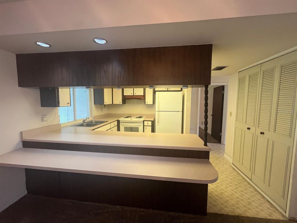 A kitchen with a breakfast bar, white appliances, and wood cabinetry viewed from a carpeted room — 13 COURTNEY PLACE, PALM COAST, FL