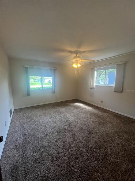 An empty bedroom with beige walls, brown carpeting, a ceiling fan, and two windows — 13 COURTNEY PLACE, PALM COAST, FL