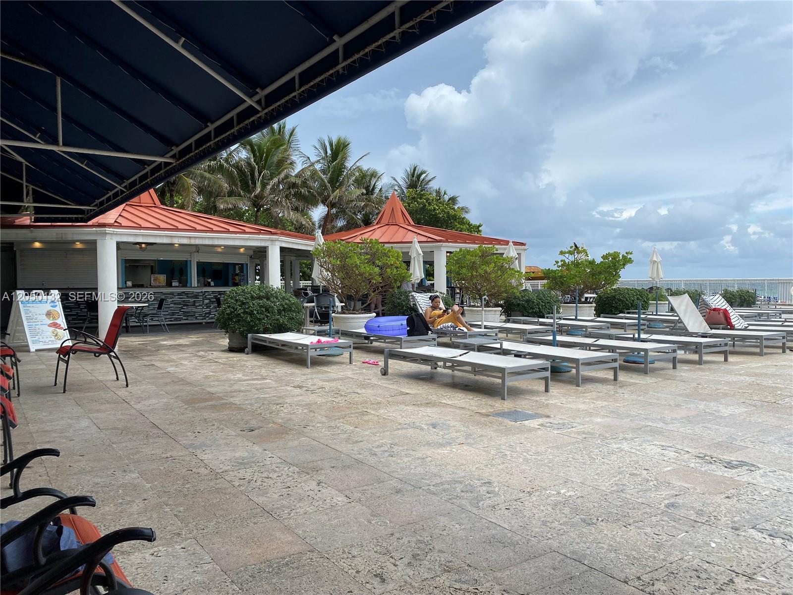 An outdoor patio area features lounge chairs, a bar with a red roof, and palm trees — 19201 E Collins Ave # 442, Sunny Isles Beach FL 33160, SUNNY ISLES BEACH, FL