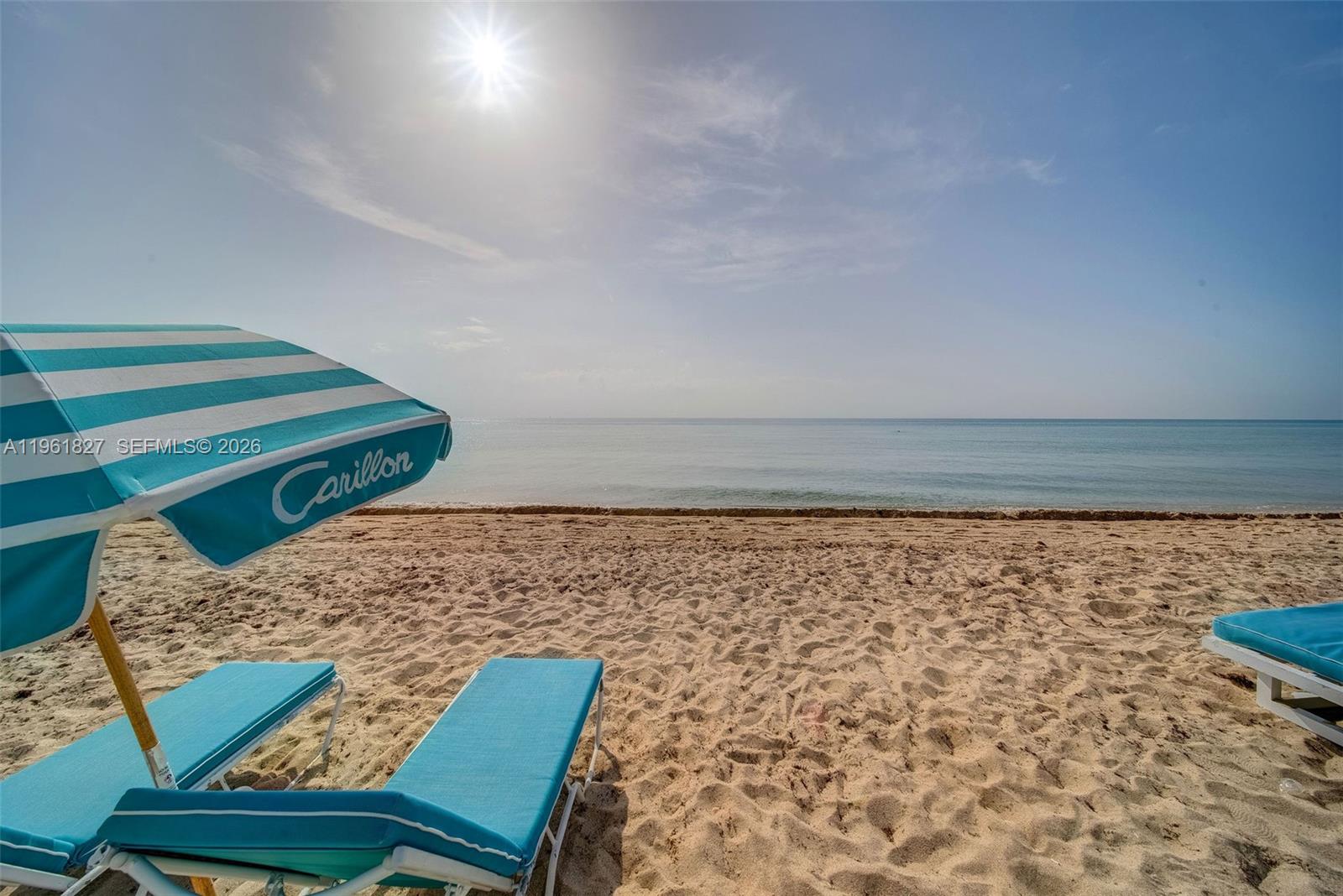 A beach scene features a blue and white striped umbrella over two lounge chairs — 6801 Collins Ave, Miami Beach FL 33141, MIAMI BEACH, FL