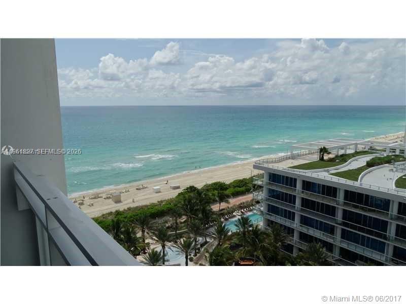 A high-angle view from a balcony overlooking a beach, ocean, and a modern building — 6801 Collins Ave, Miami Beach FL 33141, MIAMI BEACH, FL