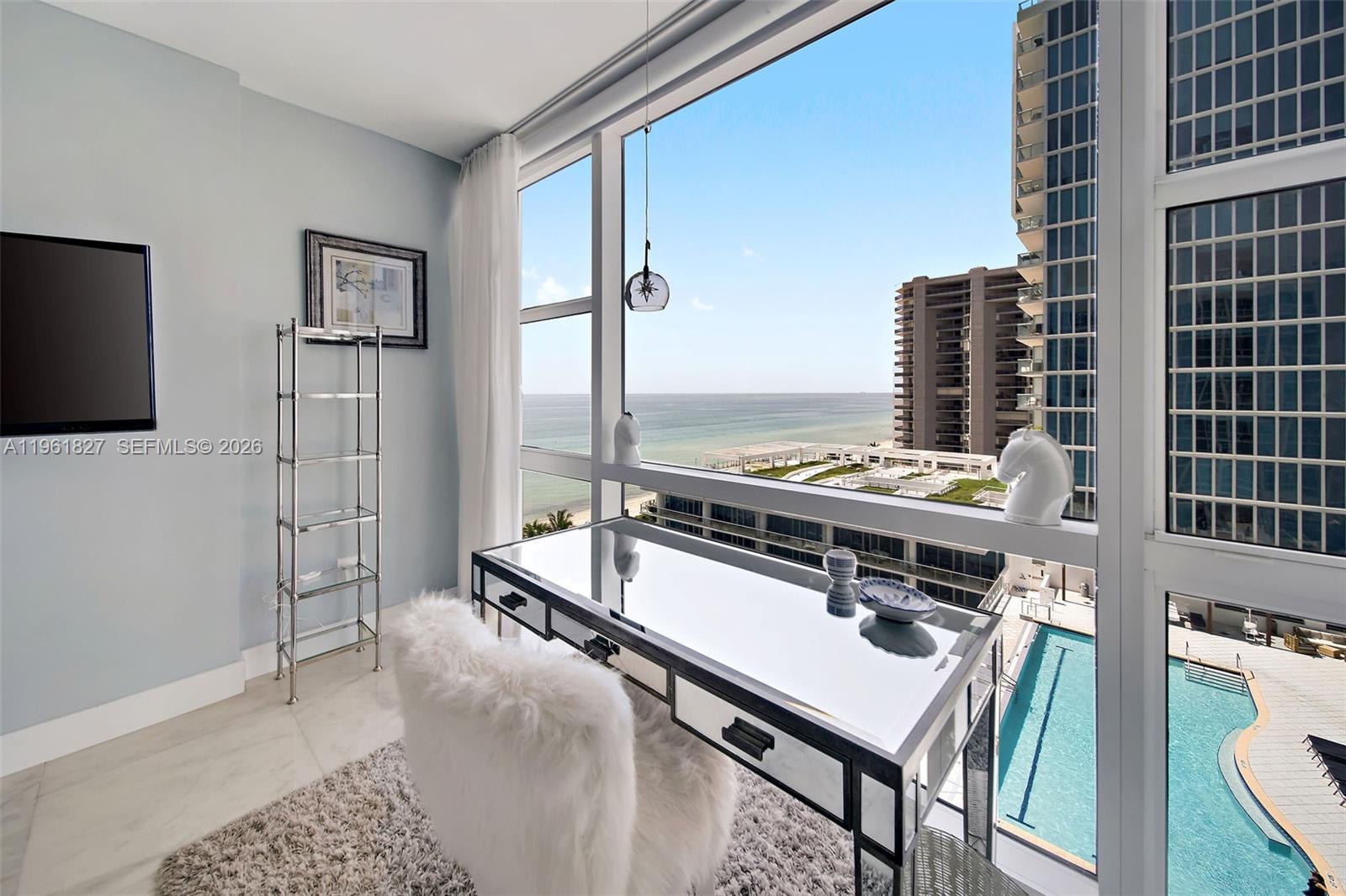 A home office features a mirrored desk, a fuzzy chair, and floor-to-ceiling windows overlooking the ocean — 6801 Collins Ave, Miami Beach FL 33141, MIAMI BEACH, FL