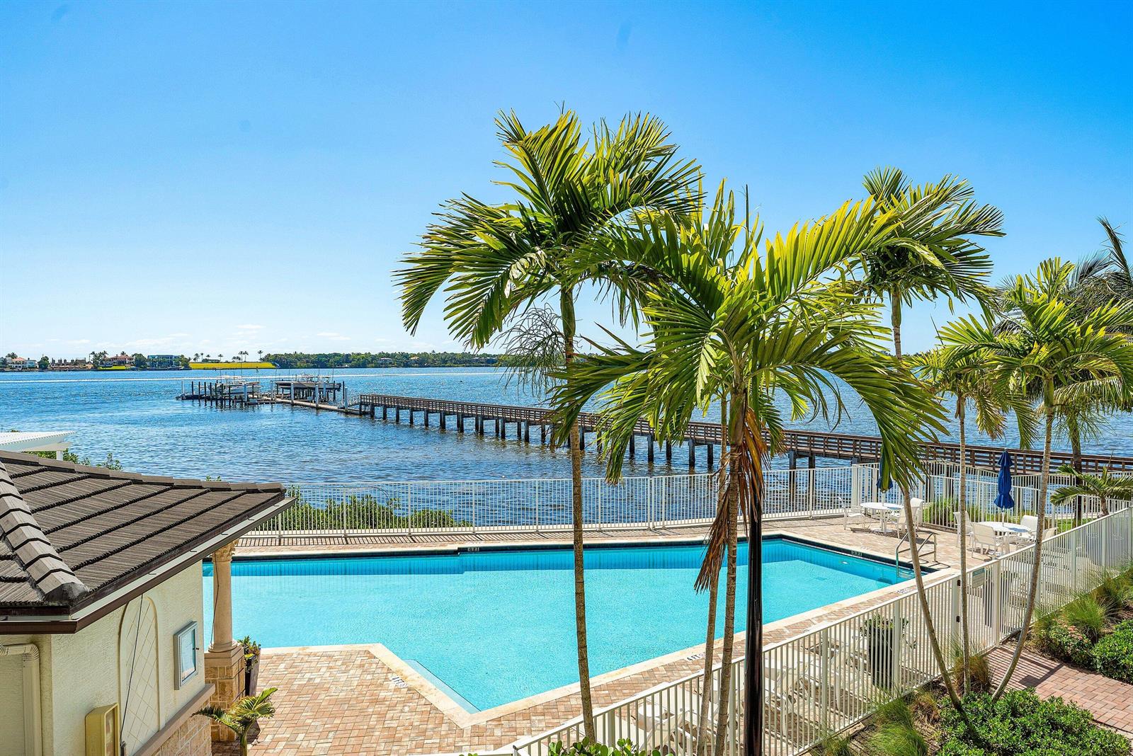 A swimming pool sits on a patio overlooking a wooden pier and a large body — 10 Windward Lane, Boynton Beach FL 33435, BOYNTON BEACH, FL