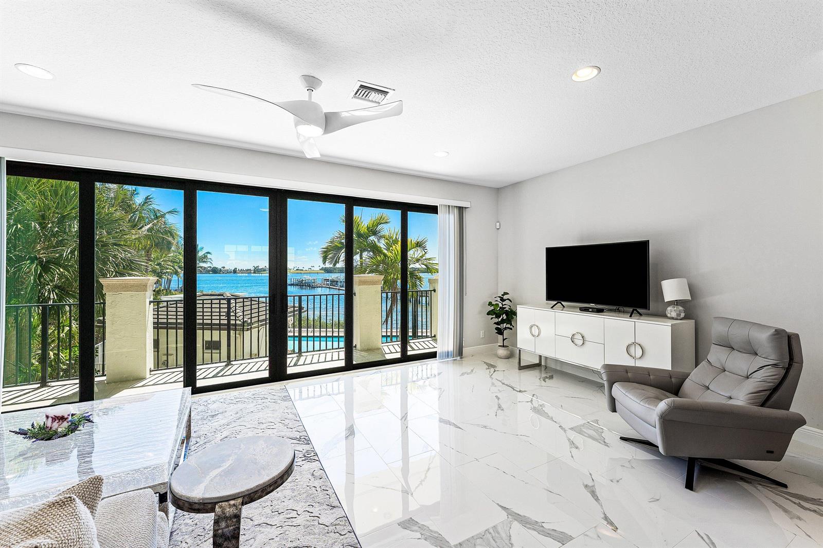 A living room with marble floors, a television console, and sliding doors overlooking the water — 10 Windward Lane, Boynton Beach FL 33435, BOYNTON BEACH, FL
